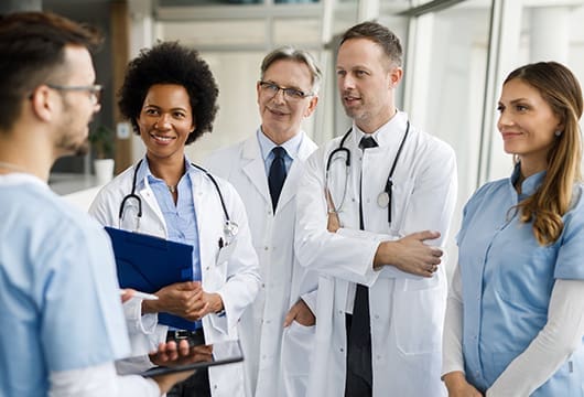 An image of a group of doctors in white lab coats conversation with another healthcare processional in scrubs holding a tablet