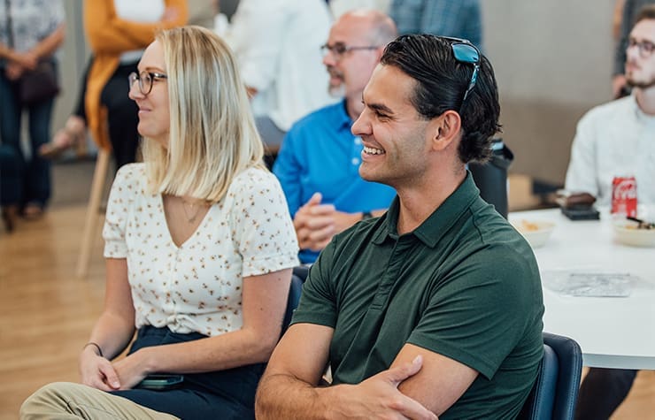 An image of a female and male coworker sitting in crowd smiling.