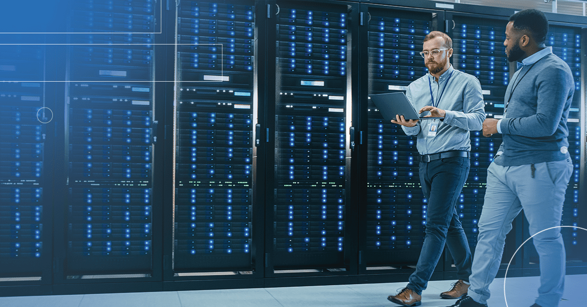 An image of two male engineers walking through the data center conversing one of them is holding a laptop