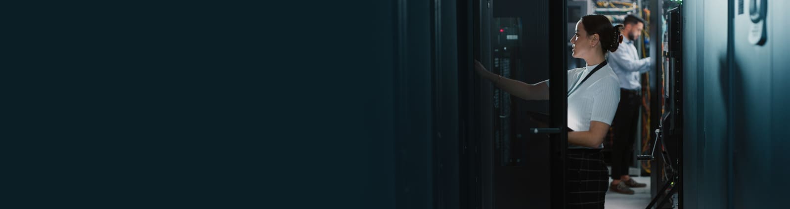 An image of a female engineer reaching into a server cabinet with a male engineer in the background inspecting equipment in a server rack