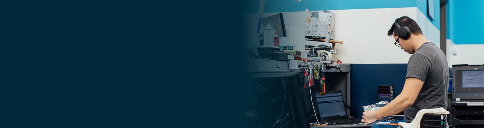 An image of a male engineer wearing headphones at a workbench testing parts