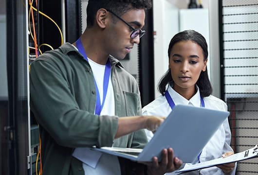 Two Engineers Wearing Lanyards Collaborate on Laptop