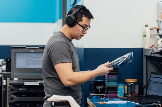 An image of an engineer wearing headphones and holding an equipment part to inspect it