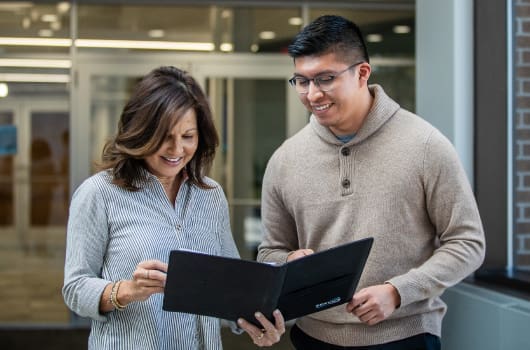 An image of a female professional with a notebook open showing a male professional the page