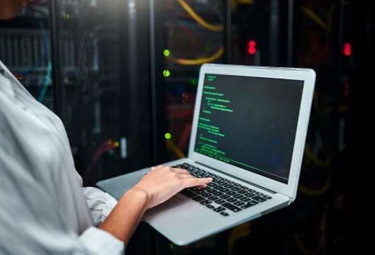 An image of hands typing at a laptop in a data center