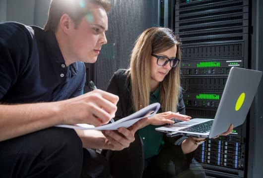 An image of a male and female engineer crouched in a data center.