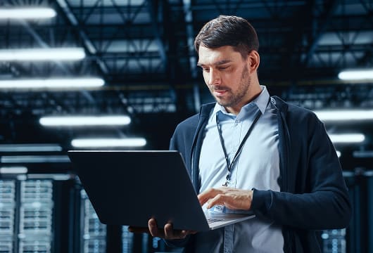 An image of an engineer in a data center holding a laptop