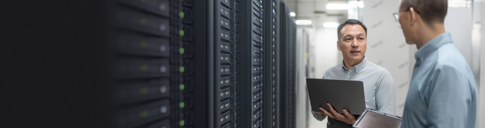 Two engineers taking in a data center one holding a laptop the other holding a tablet