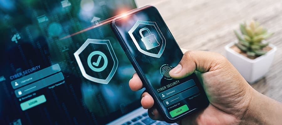An image of a hand holding a phone with a lock icon and a laptop in the background with a green checkmark icon