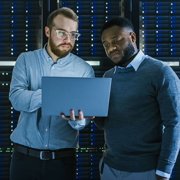Two engineers in a data center looking at a laptop one of them is holding