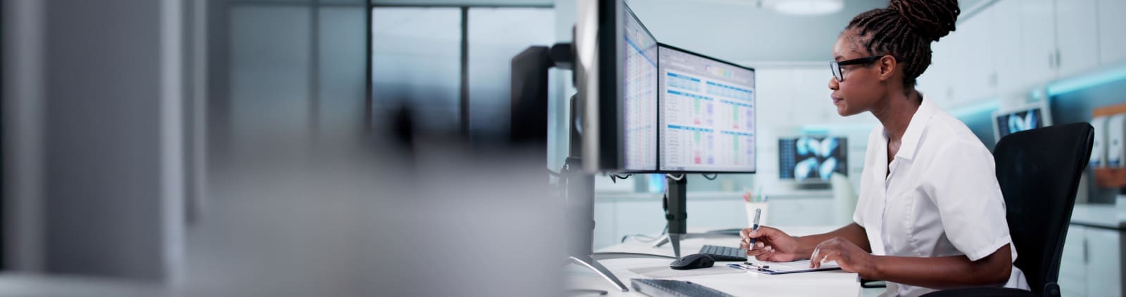 An image of a healthcare worker in front of a computer at a desk making notes