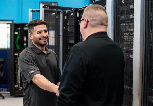 An image of two engineers shaking hands standing in a data center