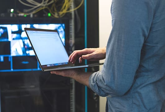 Hand Typing on Laptop Near Server