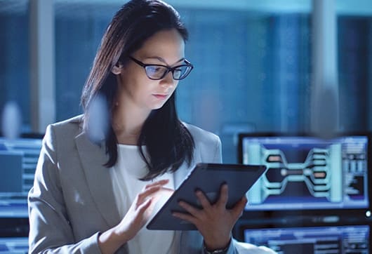 Female wearing glasses glances down at tablet.