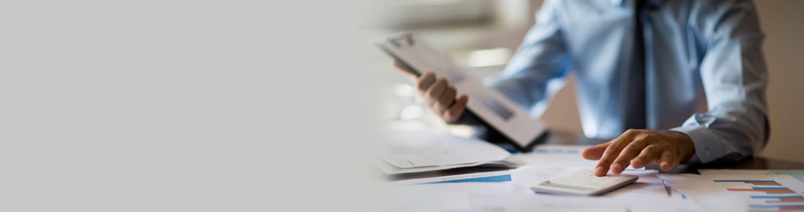 Blurred image of person in business wear typing on calculator and holding a clipboard