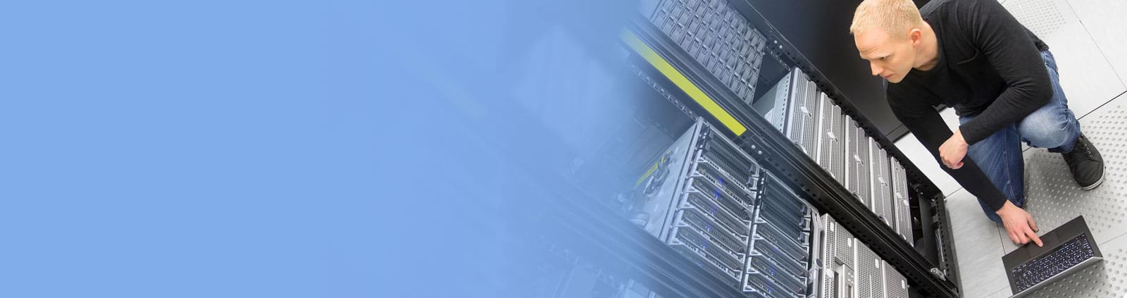 Man keeling down in data center, reaching for laptop