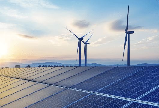 An image of wind turbines and solar panels with a sunrise on the horizon