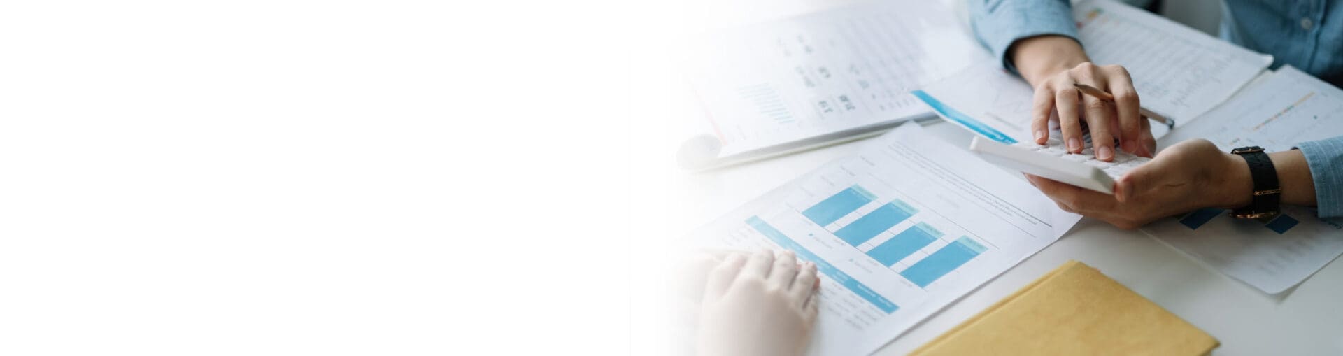 Close-up of hands typing on calculator and graphs on paper