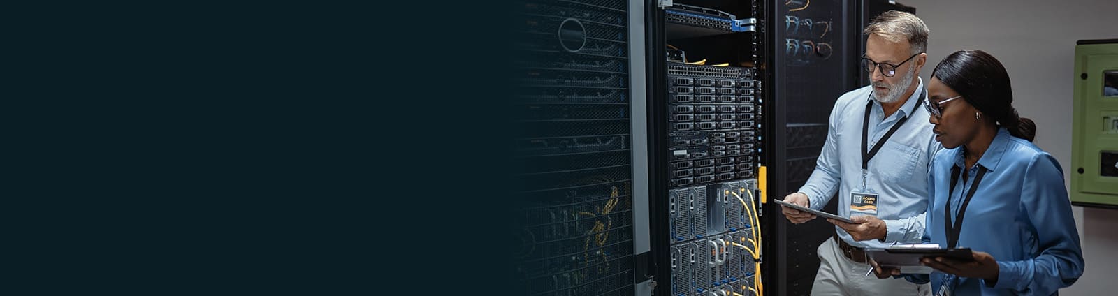 An image of two engineers in a data center inspecting equipment the female engineer is holding a clipboard, the male engineer is holding a tablet