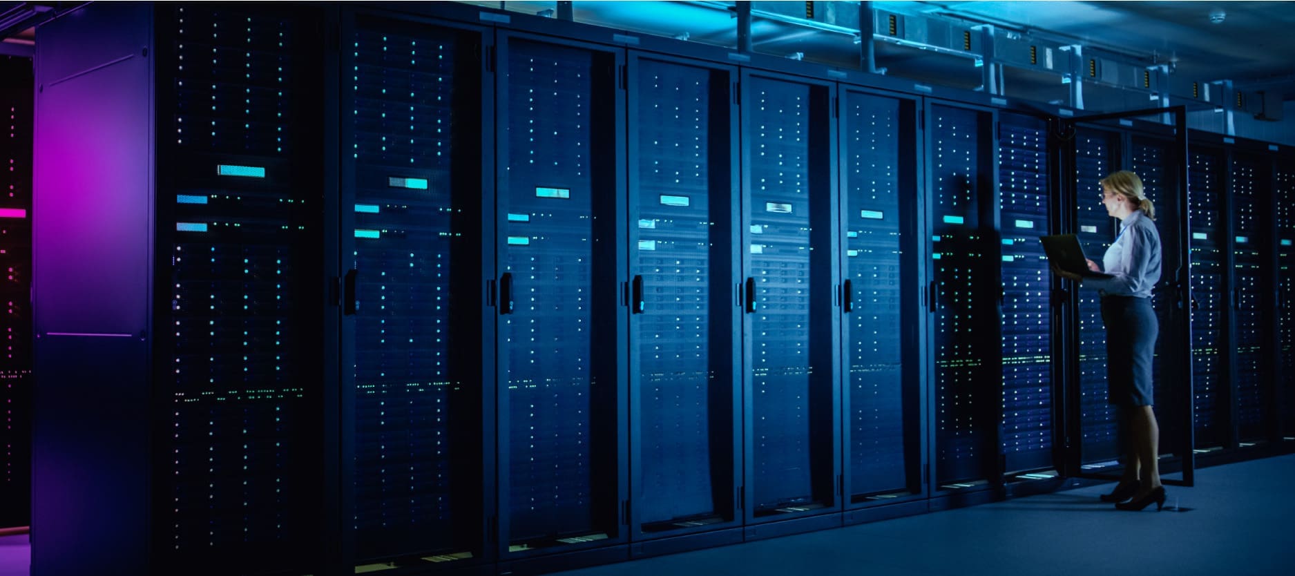 An image of a female engineer in front of an open equipment rack holding a laptop and inspecting the equipment