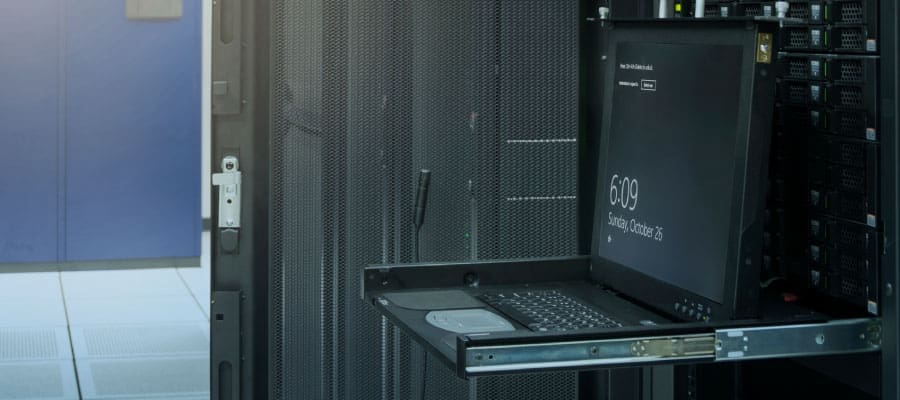 An image of a laptop open in front of an equipment rack