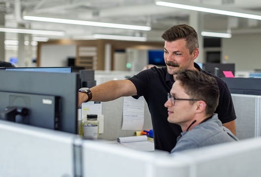 An image of two Service Express employees in a cubicle, one is pointing at the other's computer screen