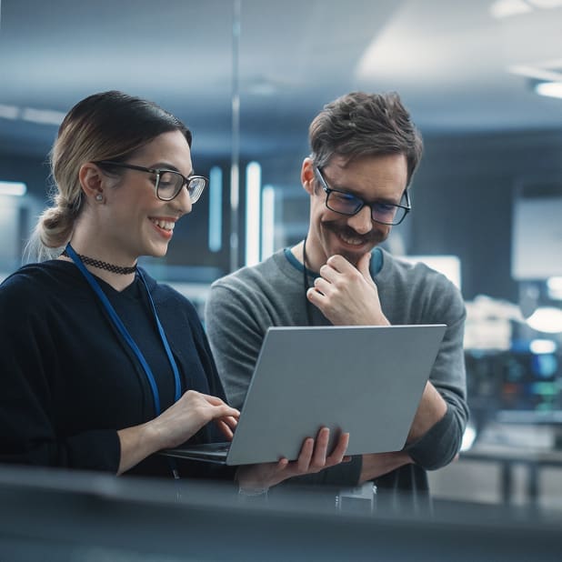 Two smiling engineers, one male, one female, looking at a laptop the female engineer is holding