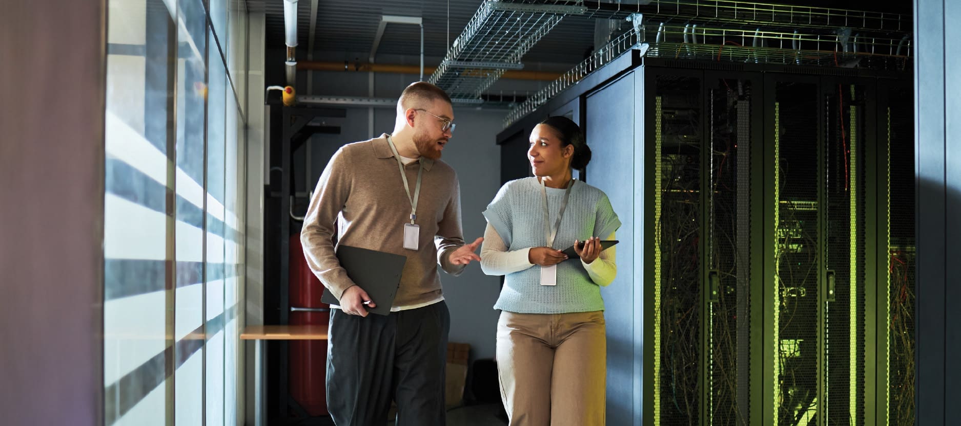 An image of a male and female engineer having a conversation while walking through a data center