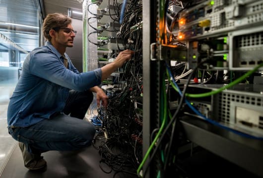 An image of an engineer kneeling in front of an equipment rack inspecting the wires